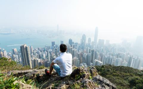 Man sitting on the top of mountain and looking cityscape/pollution