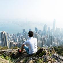 Man sitting on the top of mountain and looking cityscape/pollution