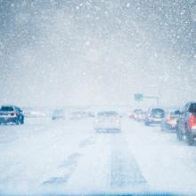 Winter weather and slow moving traffic creeping along a snow covered and icy freeway in a winter snow storm blizzard. Taillights are on in low light and low visibility road conditions. 
